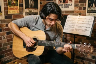 Jeune guitariste étudiant la tablature de Hallelujah de Jeff Buckley sur une guitare acoustique dans une salle de musique intimiste