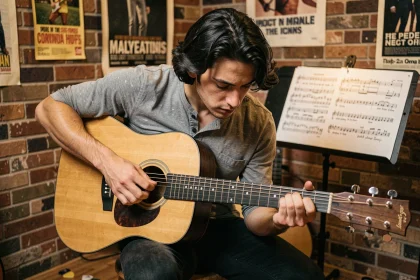 Jeune guitariste étudiant la tablature de Hallelujah de Jeff Buckley sur une guitare acoustique dans une salle de musique intimiste